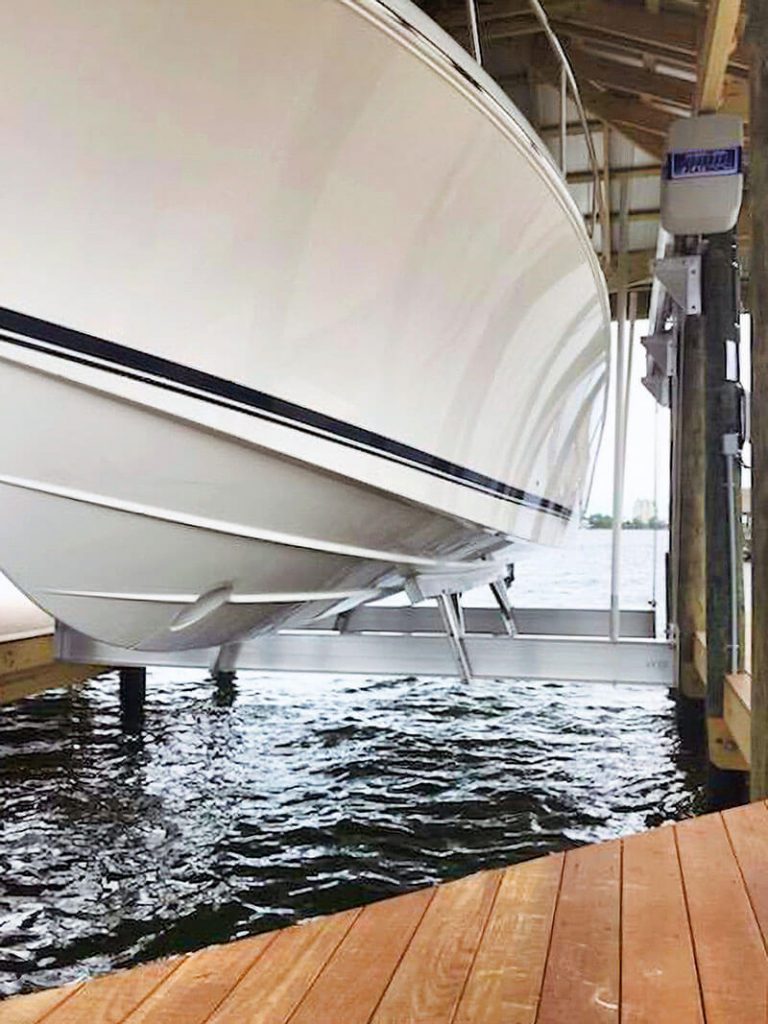 Closeup from dock of large white boat being raised from the water in an IMM Quality boat house lift
